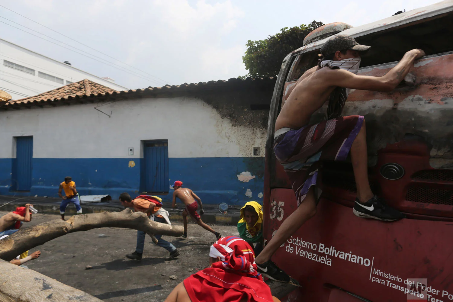 Demonstrators take cover behind a torched bus, during clashes with the Venezuelan Bolivarian National Guard in Urena, Venezuela, near the border with Colombia, Saturday, Feb. 23, 2019. (AP Photo/Rodrigo Abd)
