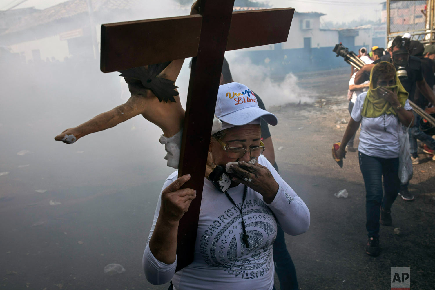  A woman carries a cross amid tear gas during clashes between the opposition and the Venezuelan Bolivarian National Guard in Urena, Venezuela, near the border with Colombia, Saturday, Feb. 23, 2019. (AP Photo/Rodrigo Abd) 