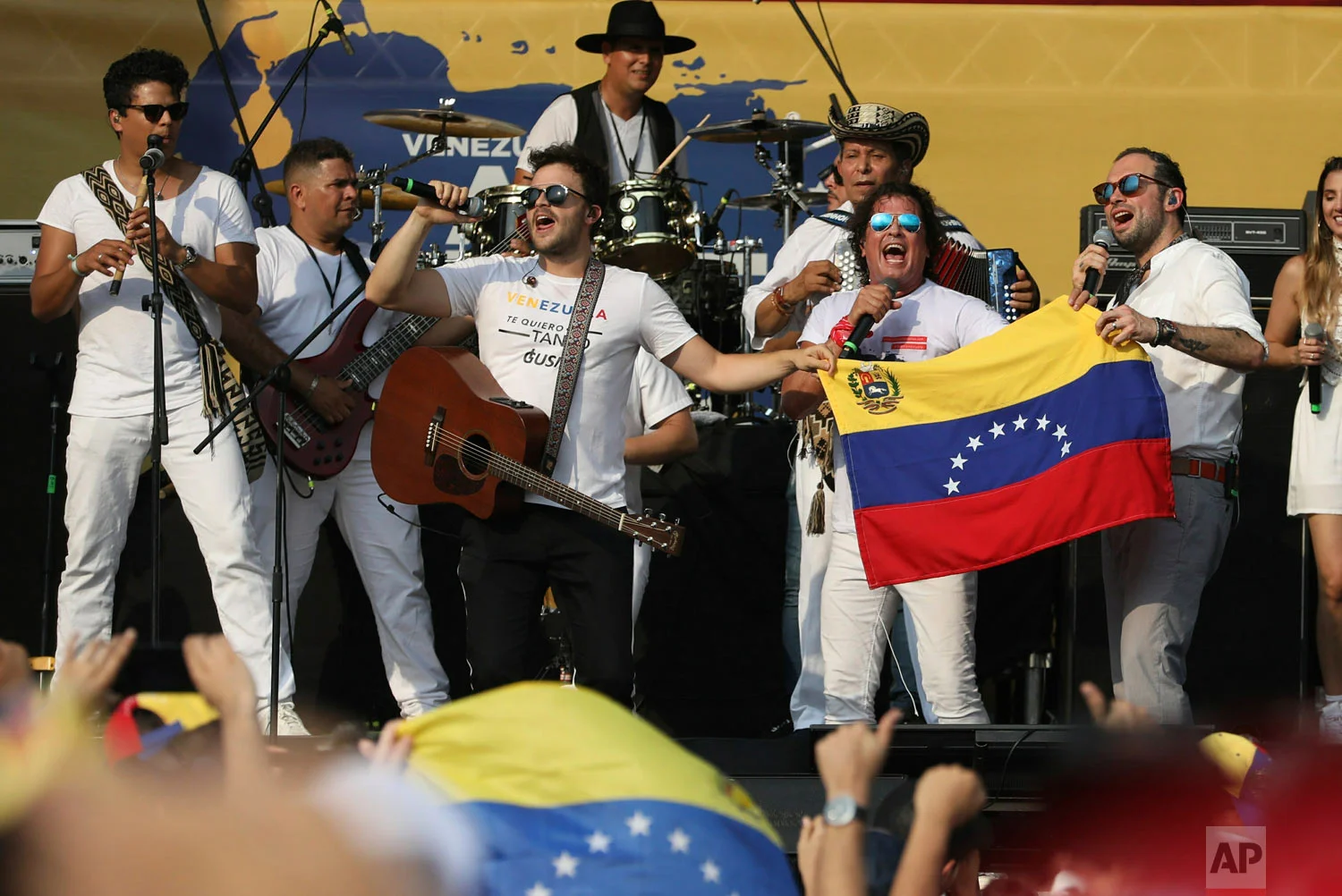 Gusi, left center, and Santiago Cruz, far right, hold a Venezuelan national flag as they perform with Carlos Vives at the Live Aid Venezuela concert at the Tienditas International Bridge on the outskirts of Cucuta, Colombia, Friday, Feb. 22, 2019, on the border with Venezuela. (AP Photo/Fernando Vergara)
