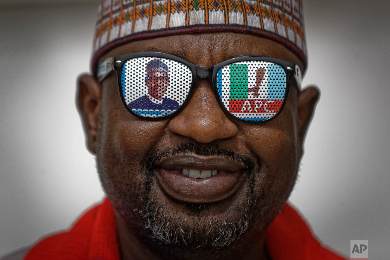 A supporter of incumbent President Muhammadu Buhari wears sunglasses with a photo of Buhari and the initials of his All Progressives Congress (APC) party, at a campaign rally in Abuja, Nigeria, Feb. 13, 2019. (AP Photo/Ben Curtis)