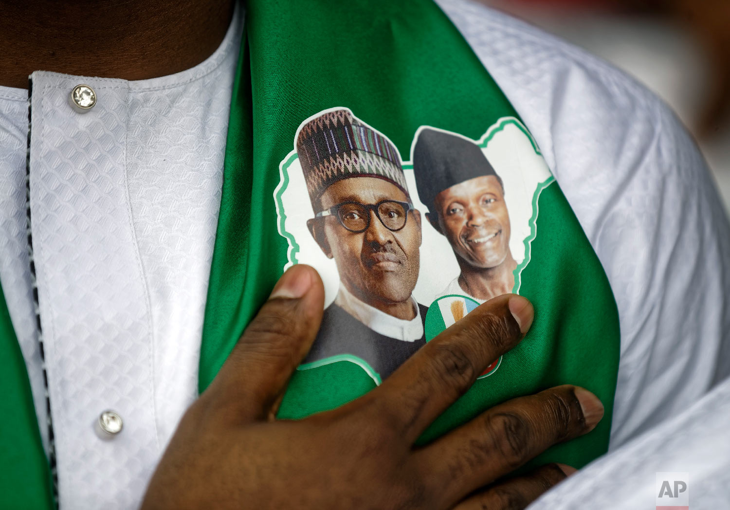 A supporter of incumbent President Muhammadu Buhari, wearing a sticker of Buhari and and Vice President Yemi Osinbajo, stands for the national anthem at a campaign rally in Abuja, Nigeria, Feb. 13, 2019. (AP Photo/Ben Curtis)