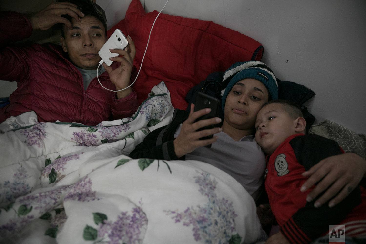  Teen Honduran migrants Josue Mejia Lucero, his girlfriend Milagro de Jesus Henriquez Ayala, 15, and Josue's 3-year-old nephew Jefferson, look at cell phones as they lie in bed at the Agape World Mission shelter in Tijuana, Mexico, Feb. 8, 2019. (AP 