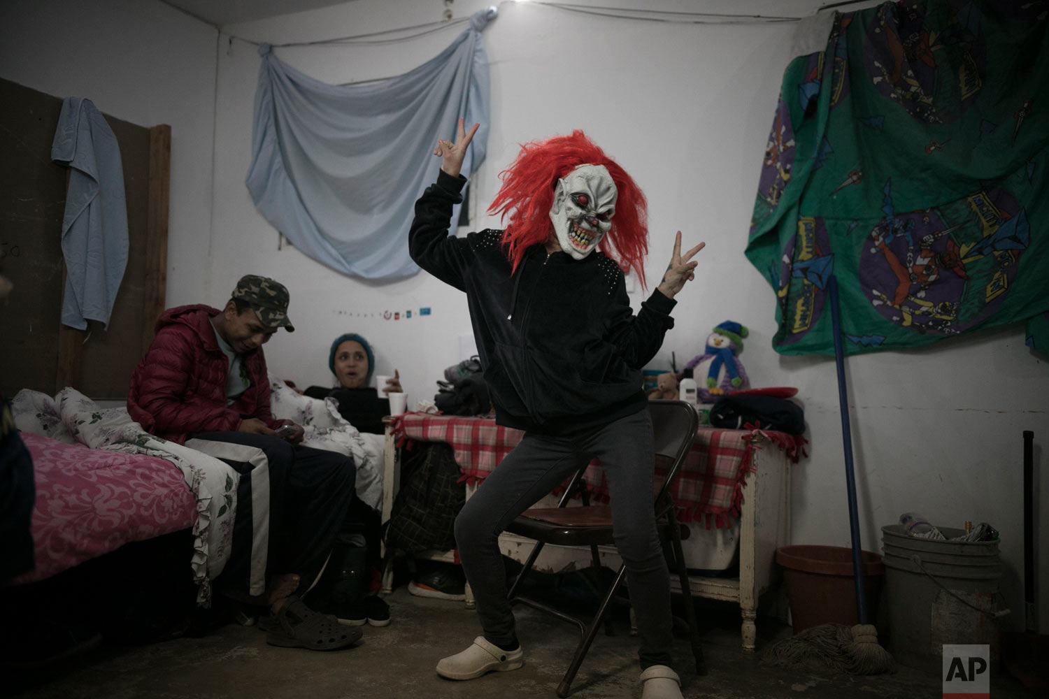  Central American teen migrants, 17-year-old Josue Mejia Lucero, left, and 15-year-old Milagro, relax on their bed as Milagro's sister Xiomara, 13, jokes around in a clown mask, at the Agape World Mission shelter where they are staying in Tijuana, Me