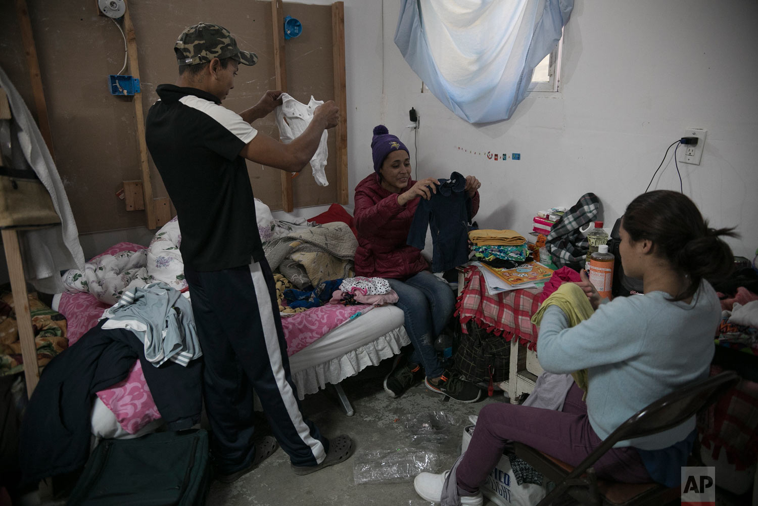  Central American migrants, 17-year-old Josue Mejia Lucero, left, 15-year-old Milagro de Jesus Henriquez Ayala, who is pregnant, center, and her younger sister Xiomara,13, organize baby clothes they selected from among donated items, in their room at