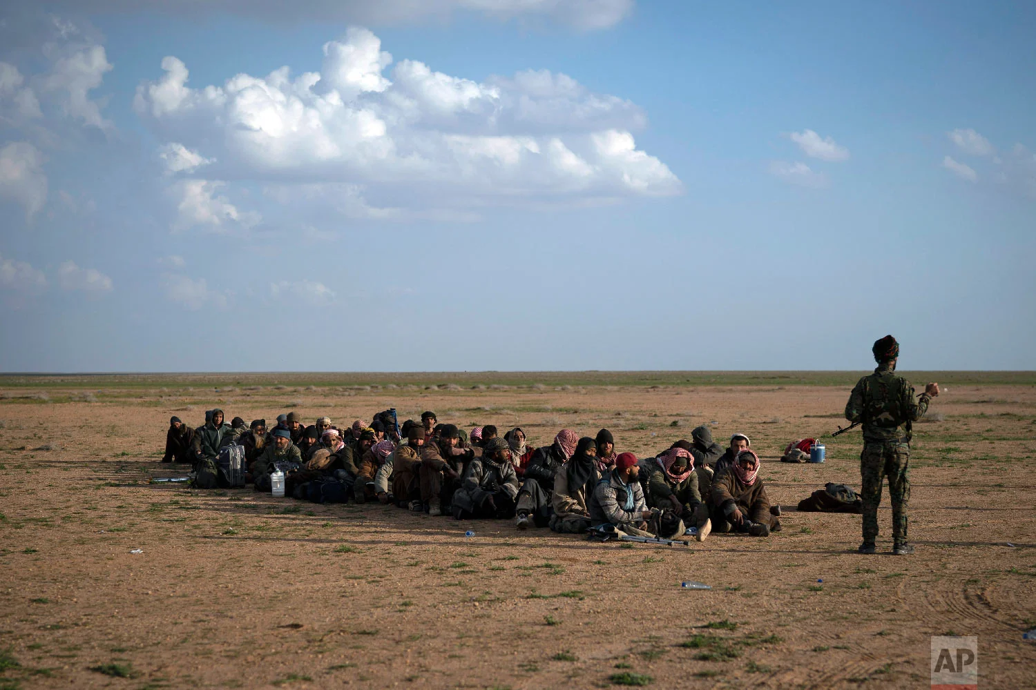  A U.S.-backed Syrian Democratic Forces (SDF) fighter stands next to a group of men, most of them foreigners, as they wait to be screened after being evacuated out of the last territory held by Islamic State militants, near Baghouz, eastern Syria, Fe