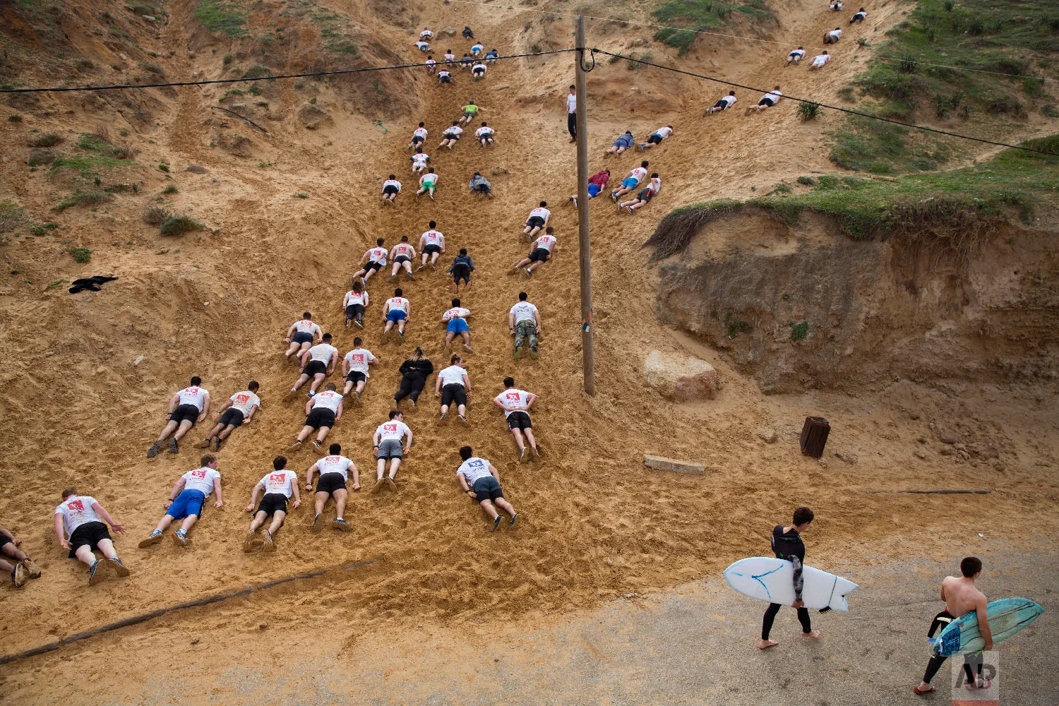  Two surfers walk towards the Mediterranean Sea as Israeli high-school seniors preparing to join the Israeli military later this year crawl out in sand dunes during an exercise at a privately run training camp for military combat fitness, in Herzliya
