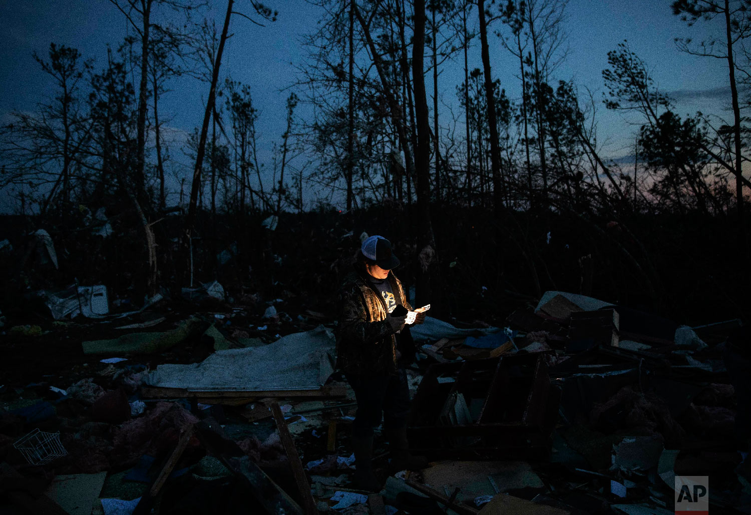 Matthew Schell looks for personal mementos by flashlight at dusk in the rubble of the house destroyed by a tornado which killed his uncle, David Wayne Dean, in Beauregard, Ala., March 4, 2019. (AP Photo/David Goldman)