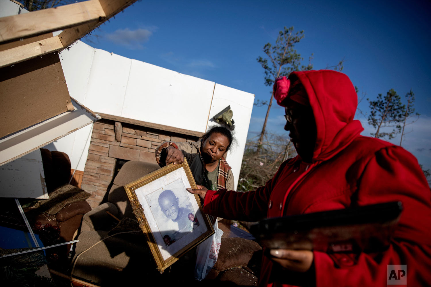 Shiraka Baker, left, passes a photo of her son to her daughter, Kiara Slater, while retrieving personal items from her damaged home where she survived a tornado a day earlier in Beauregard, Ala., March 4, 2019. (AP Photo/David Goldman)