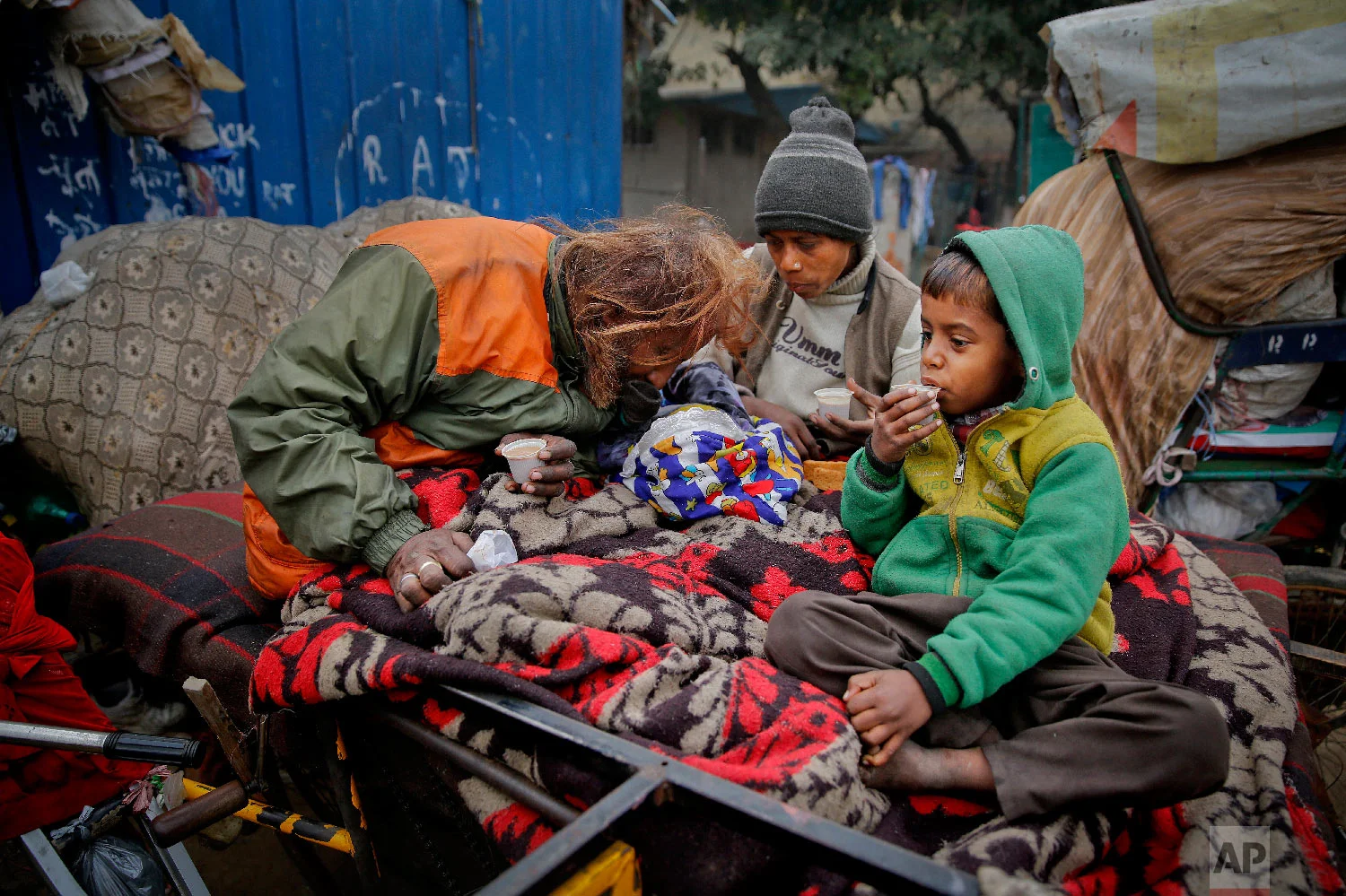 7-year-old Farmaan, right, drinks tea as his father Nasir Khan and his mother Ruby Khan tend to their three-month-old daughter Razia, while they sit on a wooden fruit vendor's cart which is their home in New Delhi, India, on Feb. 1, 2019. (AP Photo/Altaf Qadri)