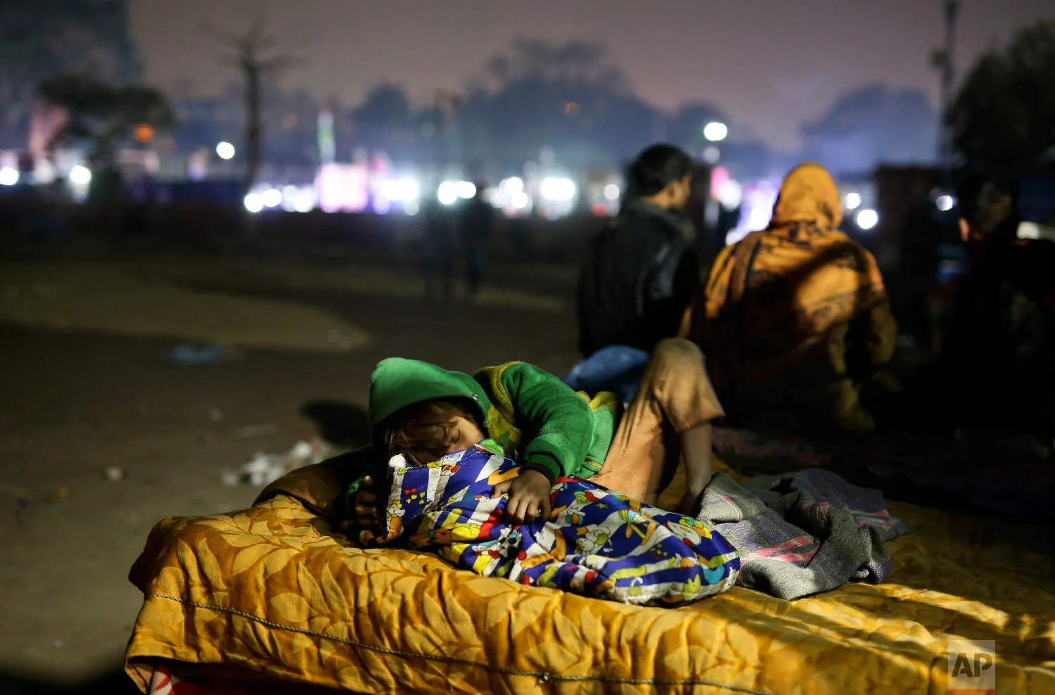 7-year-old Farmaan falls asleep while attending to his 3-month-old sister Razia, on a hand cart, which is their family's home, in New Delhi, India on Jan. 18, 2019. (AP Photo/Altaf Qadri)