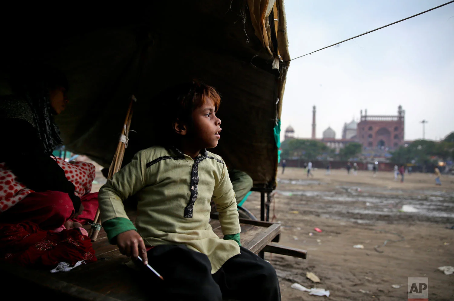 7-year-old Farmaan looks out from his home, set up on a wooden fruit vendor's cart, as it drizzles in New Delhi, India on Jan. 24, 2019, photo. (AP Photo/Altaf Qadri)