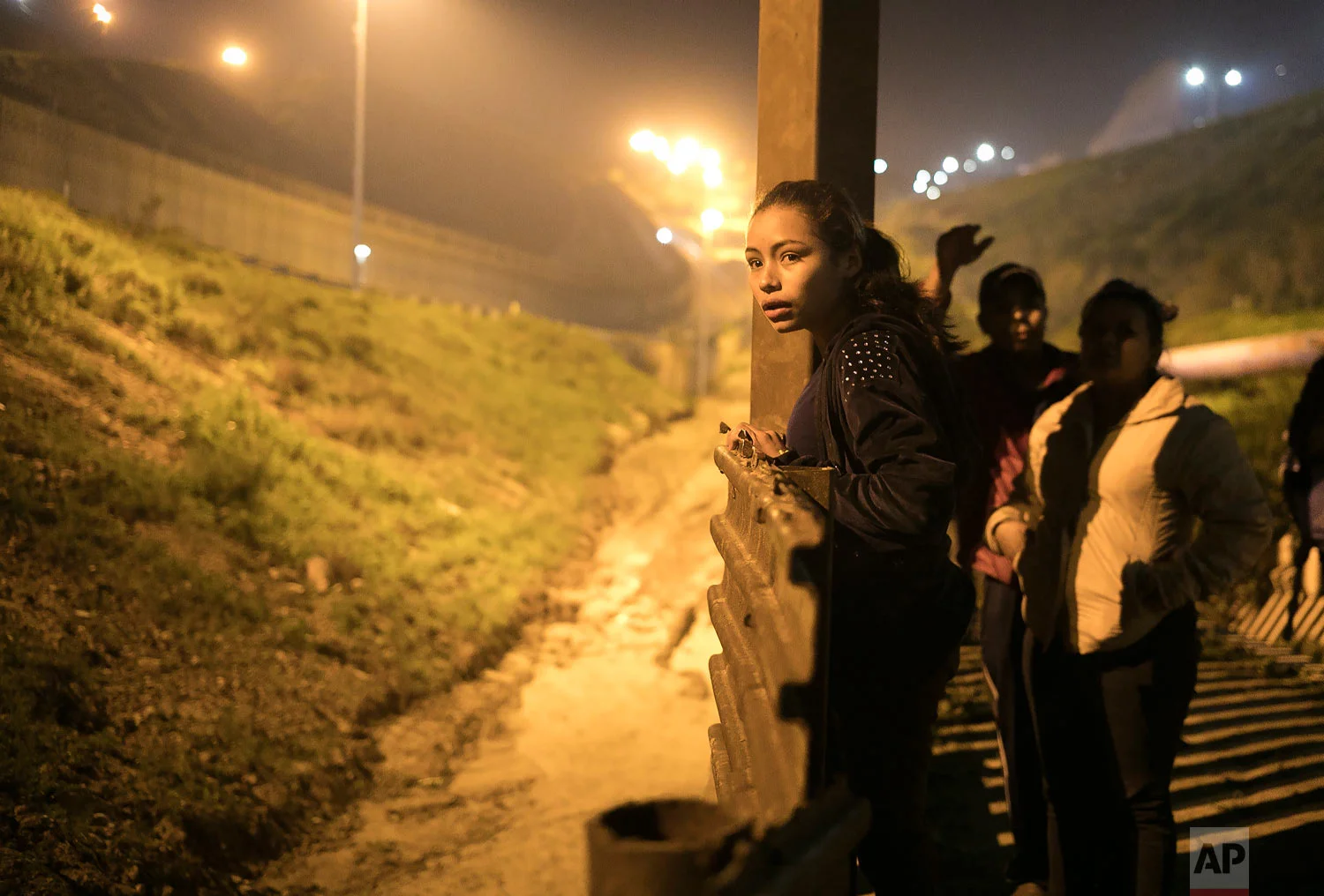 Migrant Xiomara Henriquez Ayala, 13, from El Salvador, peers over the U.S. border fence from Tijuana, Mexico, Feb. 8, 2019, next to Josue Mejia Lucero, 17, and his sister Lucero, 25, both of Honduras, as they look for a way to help Lucero and her son cross in the U.S. undetected. (AP Photo/Emilio Espejel)
