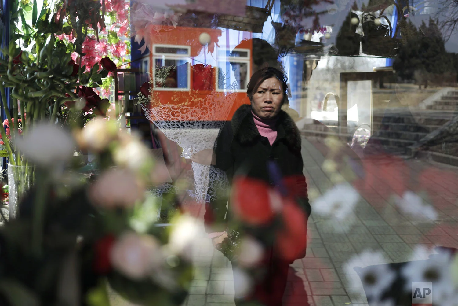 A woman's reflection is seen on the window of a kiosk that sells flowers in celebration of International Women's Day in Pyongyang, North Korea, Friday, March 8, 2019. (AP Photo/Dita Alangkara)