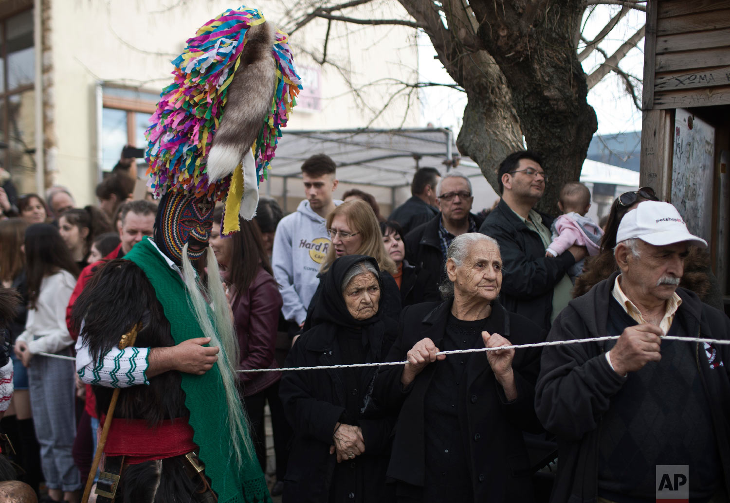 Spectators look on as a man wearing a goat hide with bells around his waist and a mask that includes a meter tall, ribbon-covered formation topped with a foxtail, also called a bell wearer, participates in a Clean Monday festival in the village of Sohos, northern Greece on March 11, 2019. (AP Photo/Petros Giannakouris)