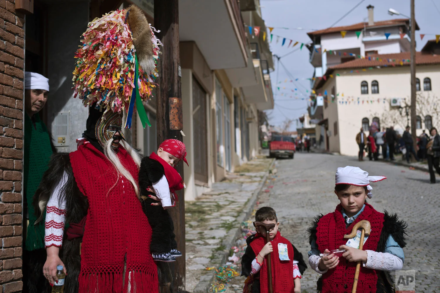 A mother wearing goat hide with bells around here waist and a mask that includes a meter tall, ribbon-covered formation topped with a foxtail, holds her baby as her five member family prepare to take part in a Clean Monday festival in the village of Sohos, northern Greece on March 11, 2019. (AP Photo/Petros Giannakouris)