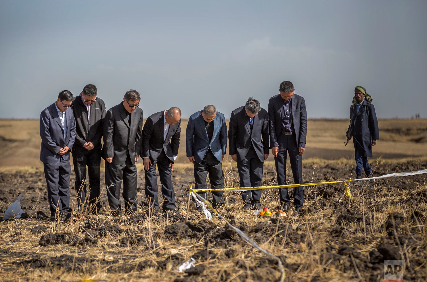 Officials from the Aviation Industry Corporation of China (AVIC) pray next to an offering of fruit, bread rolls, and a plastic container of Ethiopian Injera, a fermented sourdough flatbread, placed next to incense sticks, at the scene where the Ethiopian Airlines Boeing 737 Max 8 crashed shortly after takeoff on Sunday near Bishoftu, Ethiopia, March 12, 2019. (AP Photo/Mulugeta Ayene)