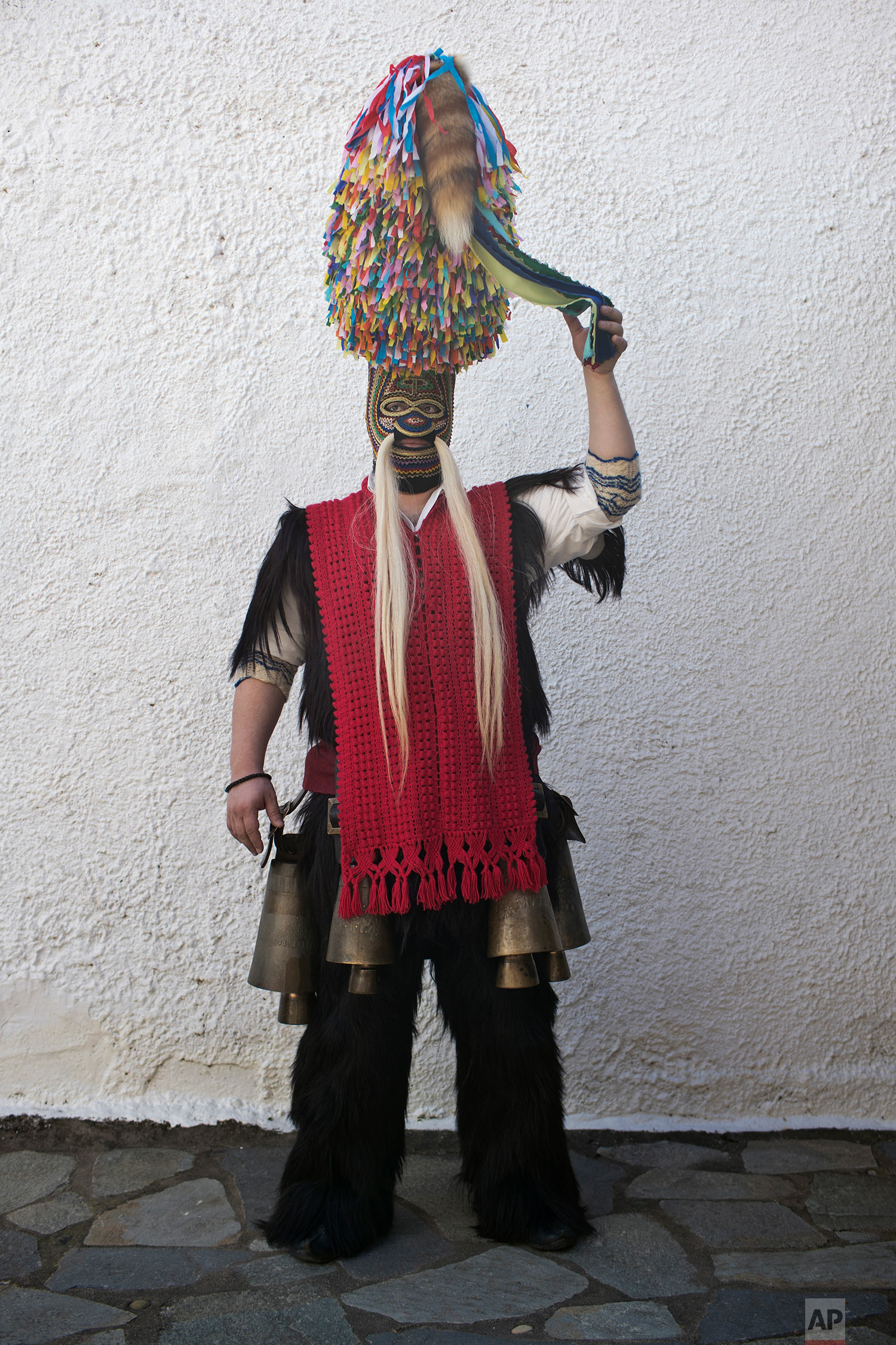  In this Monday March 11, 2019 a man wearing goat hide with bells around his waist and a mask that include a meter tall, ribbon-covered formation topped with a foxtail, also called bell wearer, poses for a picture in the village of Sohos, northern Gr