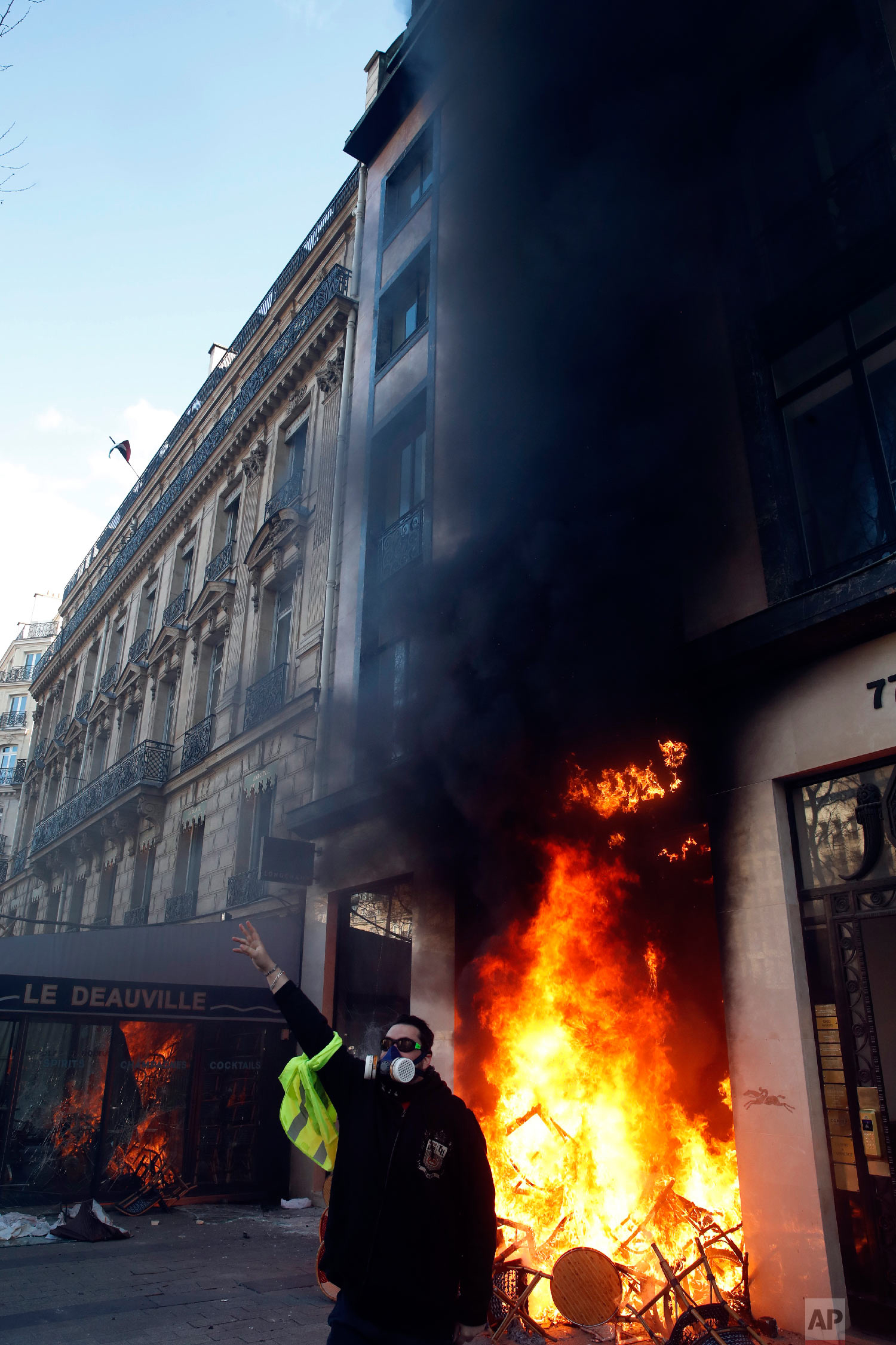 A protester stands in front of a building on fire March 16, 2019. (AP Photo/Christophe Ena)