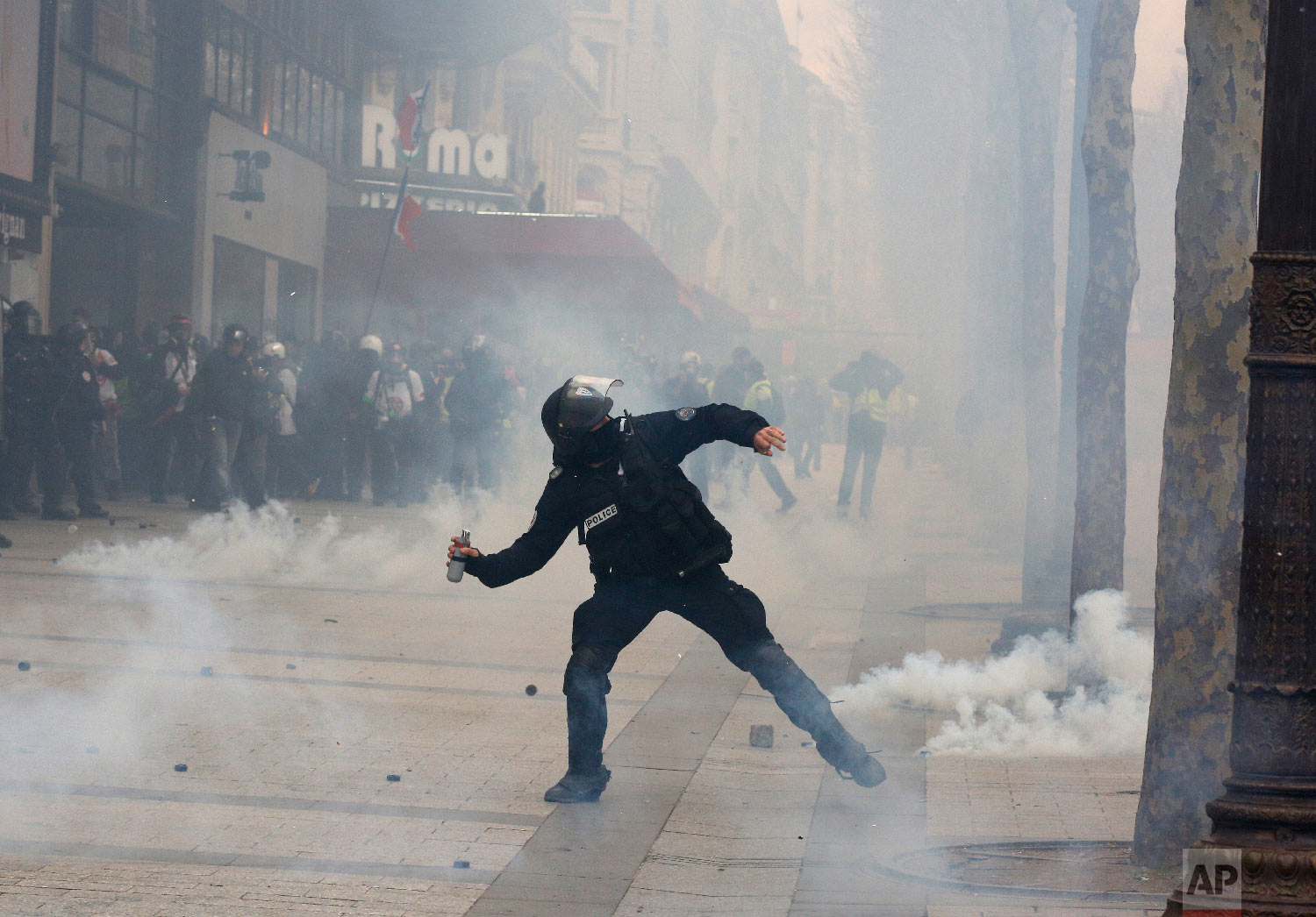 A riot police officer throws a tear gas canister onto protesters during a yellow vests demonstration March 16, 2019. (AP Photo/Christophe Ena)
