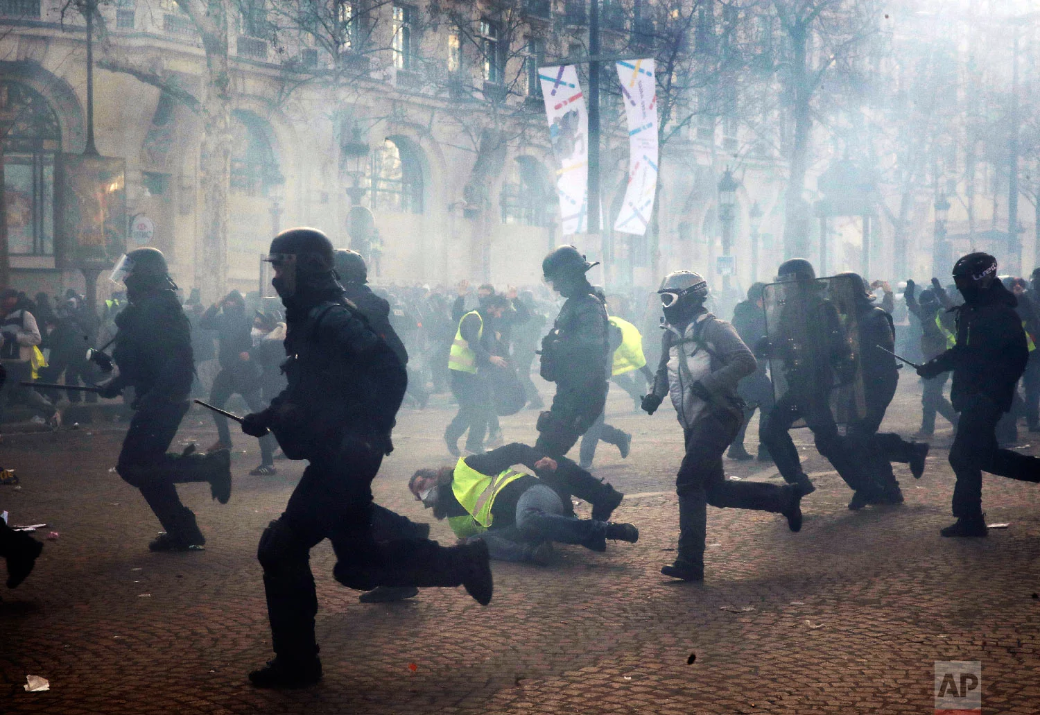 Riot police officers charge as a yellow vests demonstrator falls Saturday, March 16, 2019 in Paris. (AP Photo/Christophe Ena)