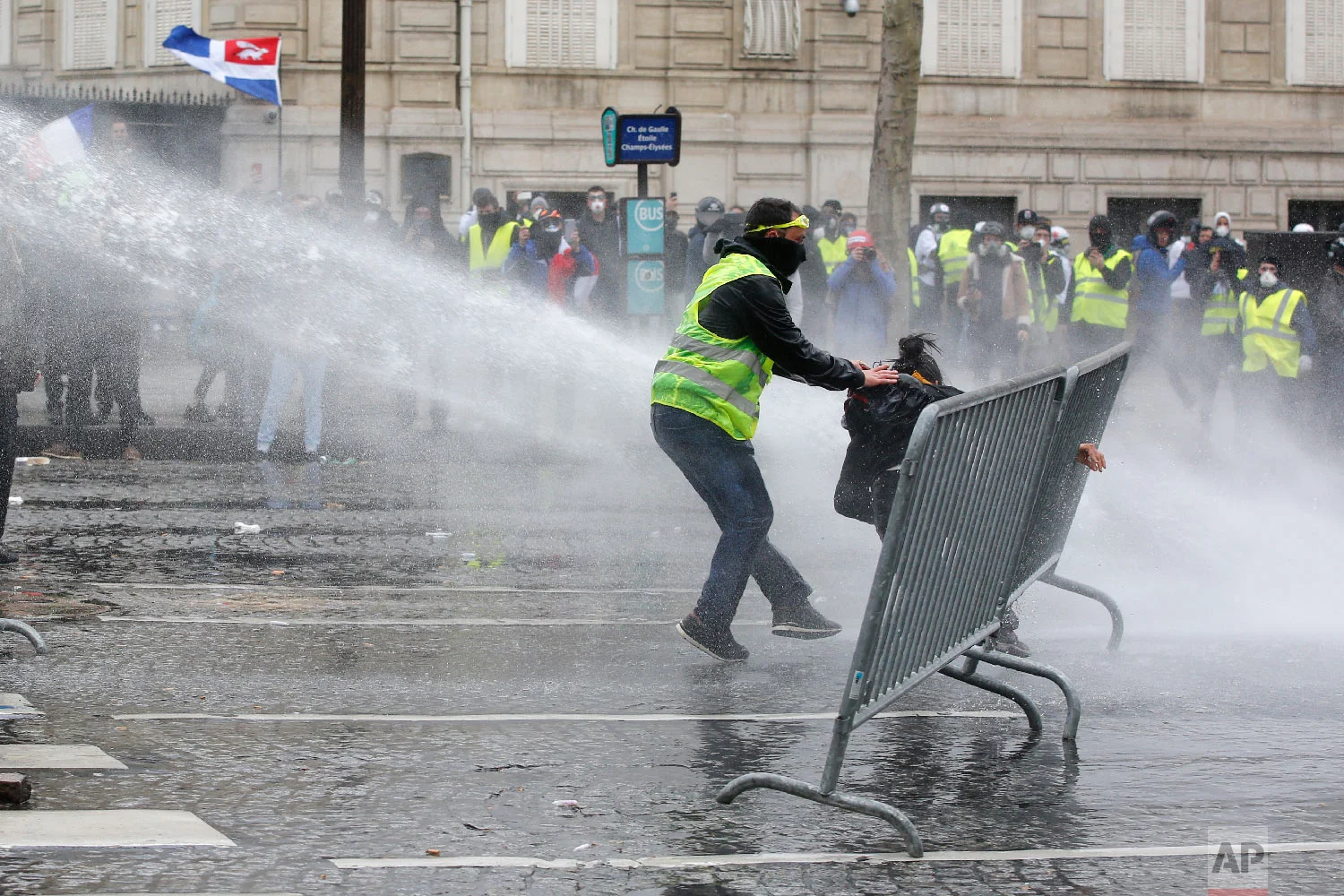 A yellow vests demonstrator rescues another one as police forces use water cannons, March 16, 2019, in Paris. (AP Photo/Christophe Ena)