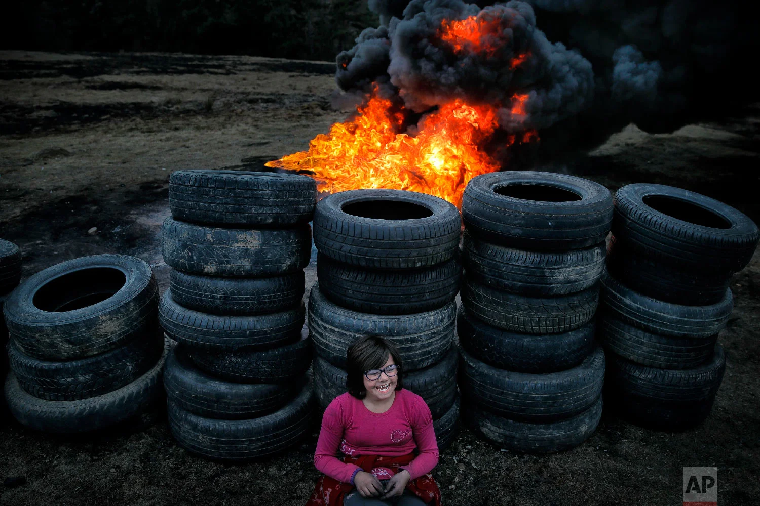 A little girl rests leaning against used tires during a ritual marking the upcoming Clean Monday, the beginning of the Great Lent, 40 days ahead of Orthodox Easter, on the hills surrounding the village of Poplaca, in central Romania's Transylvania region, Sunday, March 10, 2019. (AP Photo/Vadim Ghirda)
