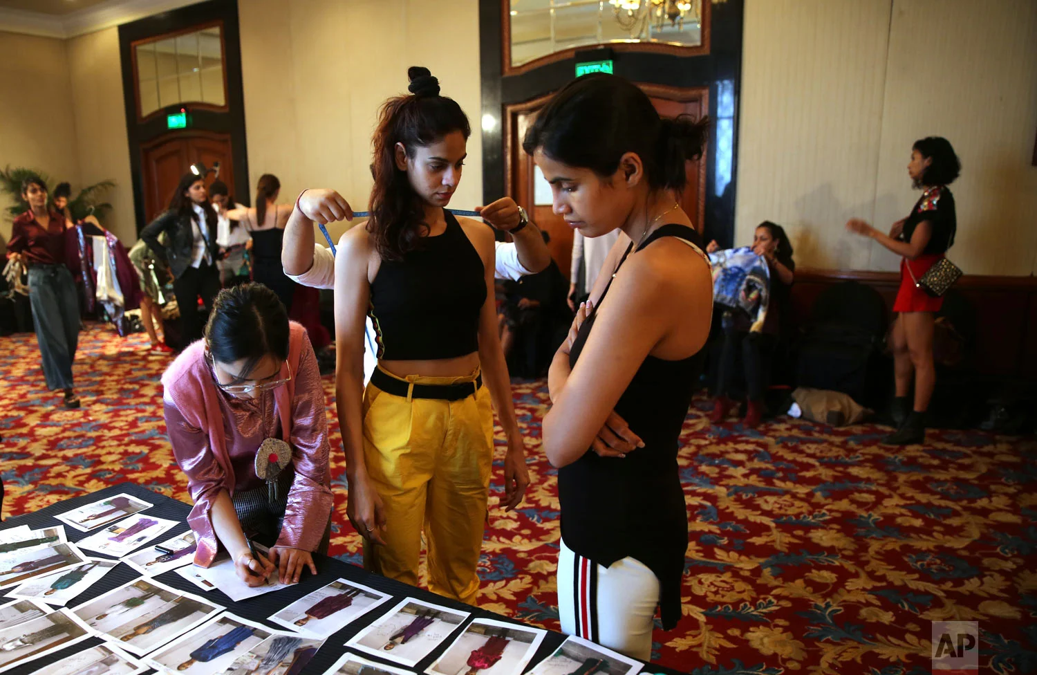A tailor takes the measurements of a model as a woman scans photographs during a fitting session ahead of the Lotus Makeup India Fashion Week, Monday, March 11, 2019, in New Delhi, India. (AP Photo/Manish Swarup)