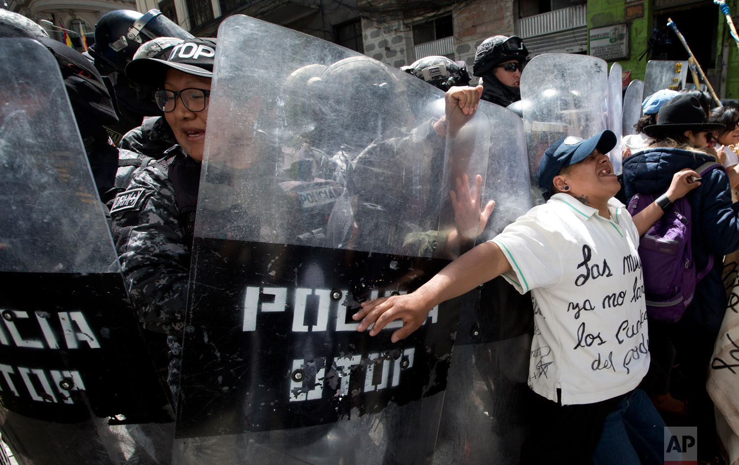 In this March 8, 2019 photo, a woman pushes against riot police who are preventing demonstrators from reaching government palace during a march marking International Women’s Day, in La Paz, Bolivia. (AP Photo/Juan Karita)