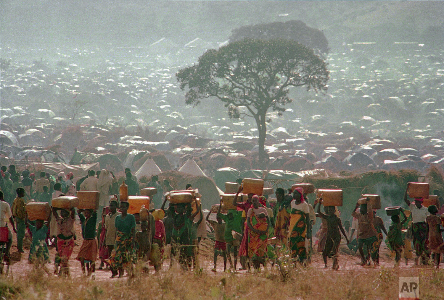 Refugees who fled the ethnic bloodbath in neighboring Rwanda carry water containers back to their huts at the Benaco refugee camp in Tanzania, near the border with Rwanda on May 17, 1994. With a population surpassing 300,000, aid agencies are having difficulty feeding, treating and sheltering them. (AP Photo/Karsten Thielker)