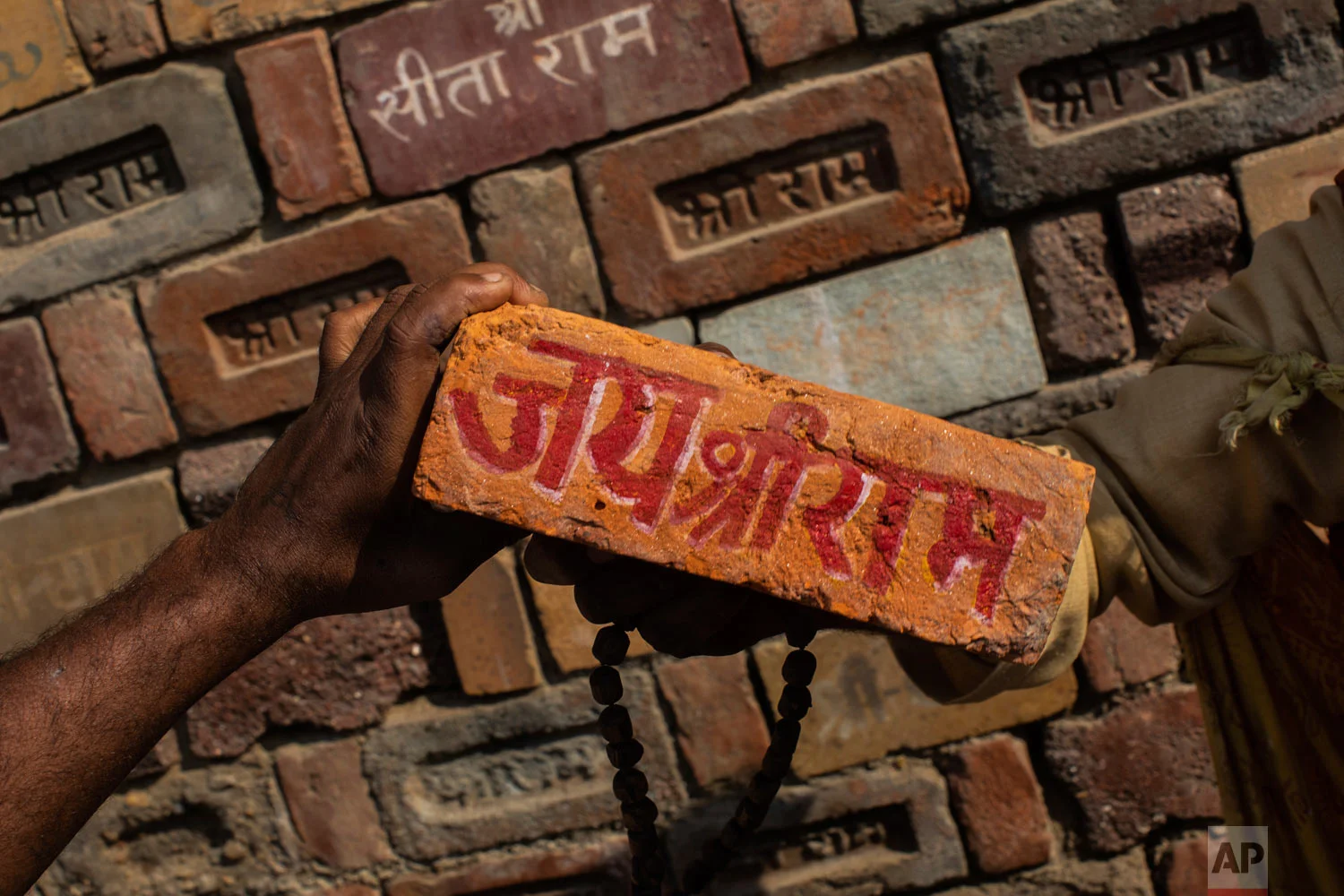 A man holds a brick reading "Jai Shree Ram" (Victory to Lord Ram) as bricks of the old Babri Mosque are piled up in Ayodhya Uttar Pradesh, India, Nov. 25, 2018. (AP Photo/Bernat Armangue)