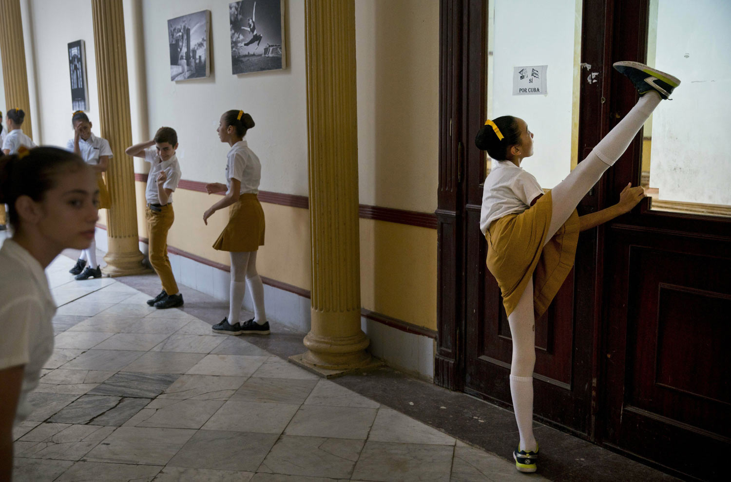 A young dancer stretches as fellow students wait for the start of a news conference on the International Meeting of Academies for the teaching of ballet, at the Fernando Alonso National Ballet School, in Havana, Cuba, on Friday, April 5, 2019. The organization's 25th edition will take place in Havana from April 13-27, with participants from the U.S., Latin America and Europe. (AP Photo/Ramon Espinosa)