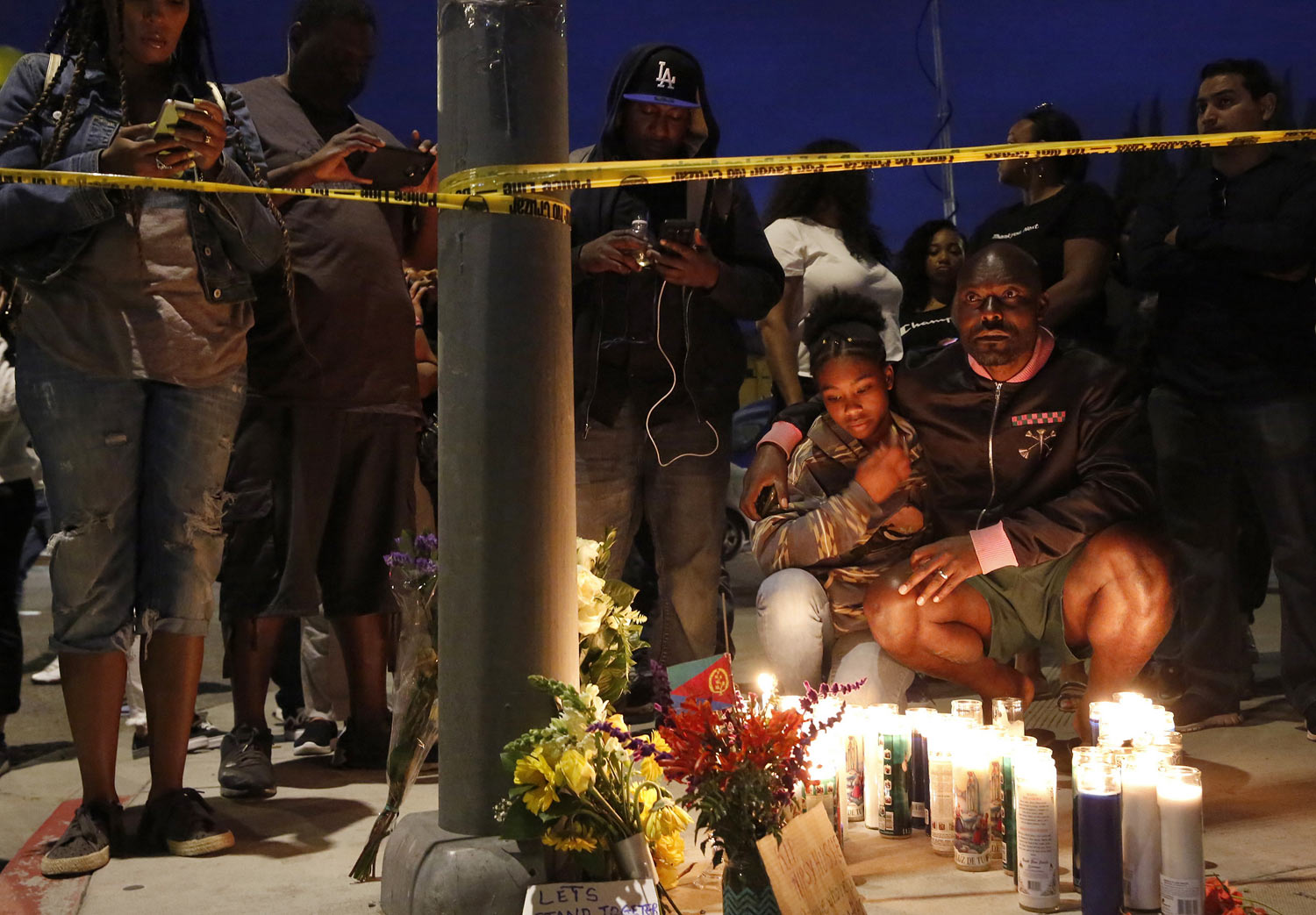 Haitian-French actor Jimmy Jean-Louis and his daughter Jasmin, 16, gather around candles set up across from the clothing store of rapper Nipsey Hussle in Los Angeles, on Sunday, March 31, 2019. Hussle, the skilled and respected West Coast rapper who had a decade-long success with mixtapes but hit new heights with his Grammy-nominated major-label debut album in 2018, was killed at the age of 33. (AP Photo/Damian Dovarganes)
