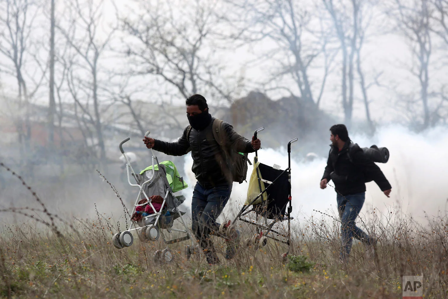 A man holding two baby strollers runs to avoid tear gas thrown by riot police during clashes outside a refugee camp in the village of Diavata, west of Thessaloniki, northern Greece, Friday, April 5, 2019. (AP Photo/Giannis Papanikos)