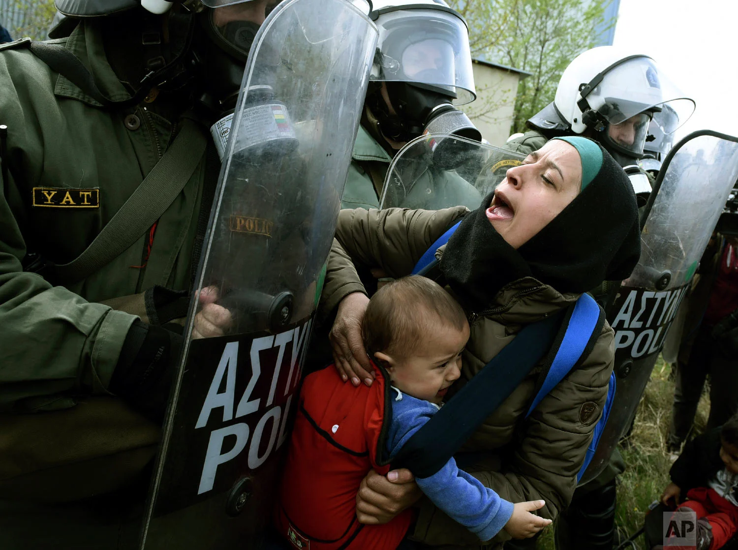 A migrant woman with a child pushing with riot police outside a refugee camp in the village of Diavata, west of Thessaloniki, northern Greece, Friday, April 5, 2019. (AP Photo/Giannis Papanikos)