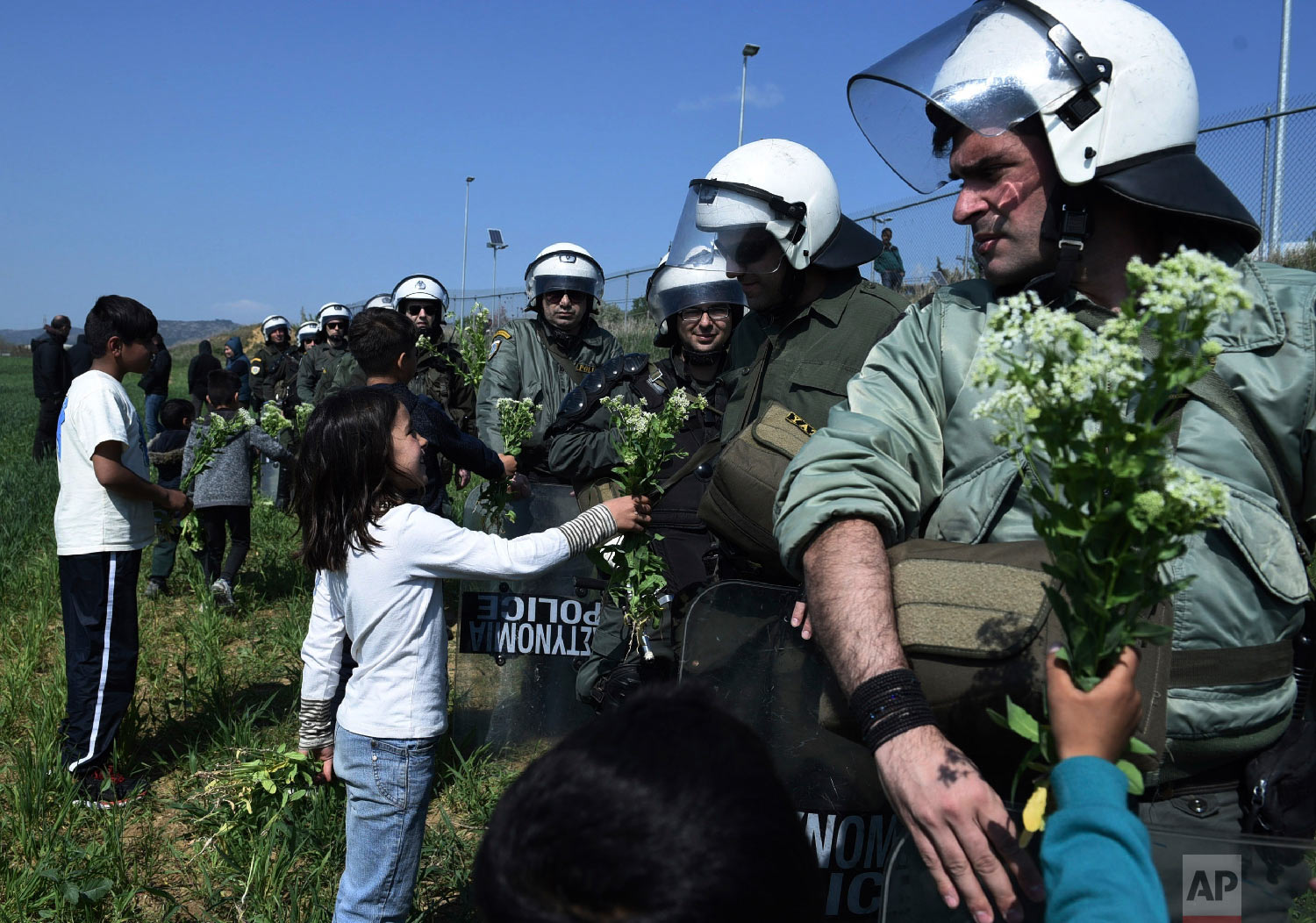 Children of migrants offer flowers to riot police during a rally outside a refugee camp in the village of Diavata, west of Thessaloniki, northern Greece, Thursday, April 4, 2019. (AP Photo/Giannis Papanikos)