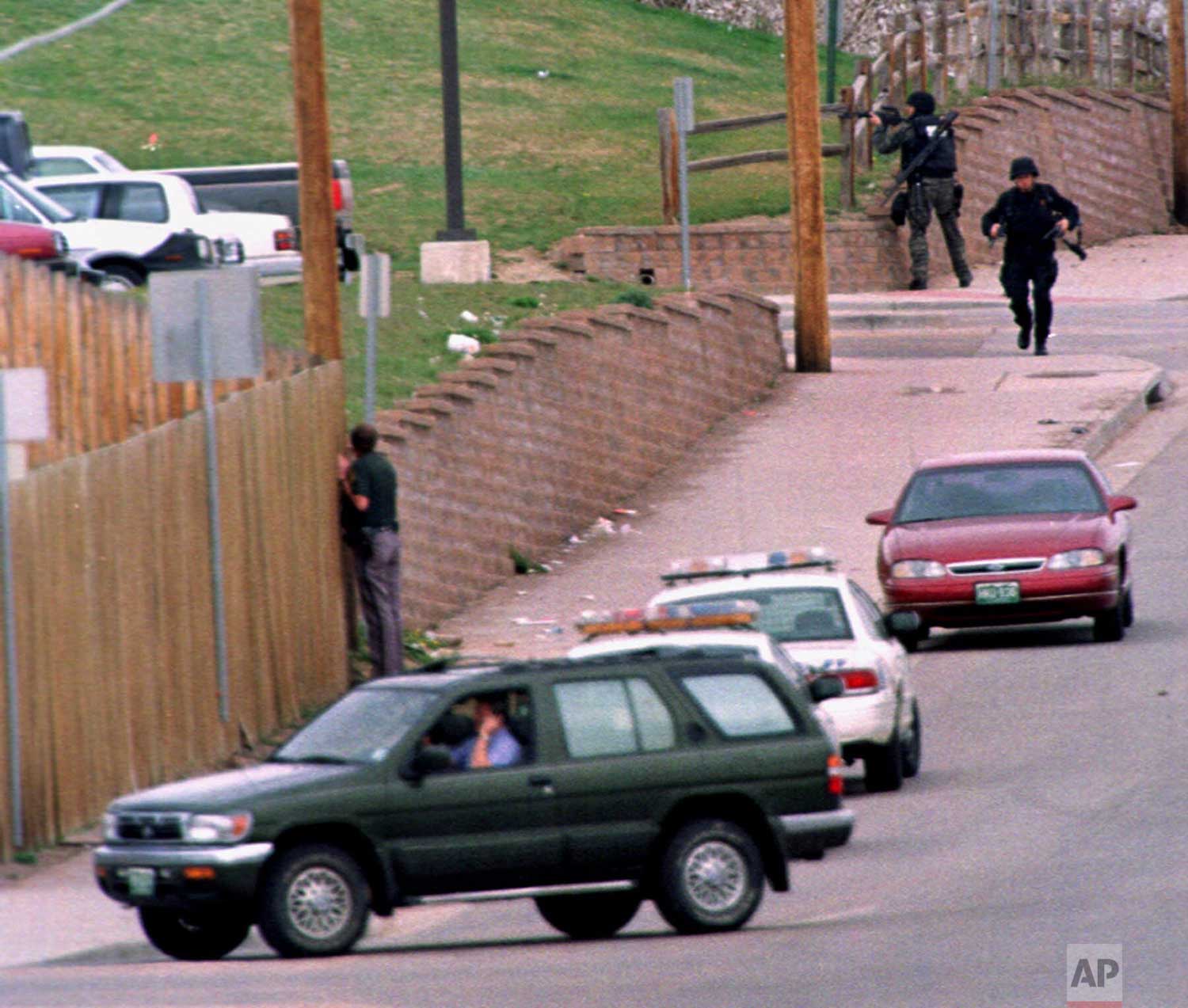  SWAT members run down Pierce Street while a Jefferson County, Colo., Sheriff's Department deputy peers through a fence to keep an eye on Columbine High School after a pair of gunmen went on a shooting rampage inside the facility, Tuesday, April 20, 