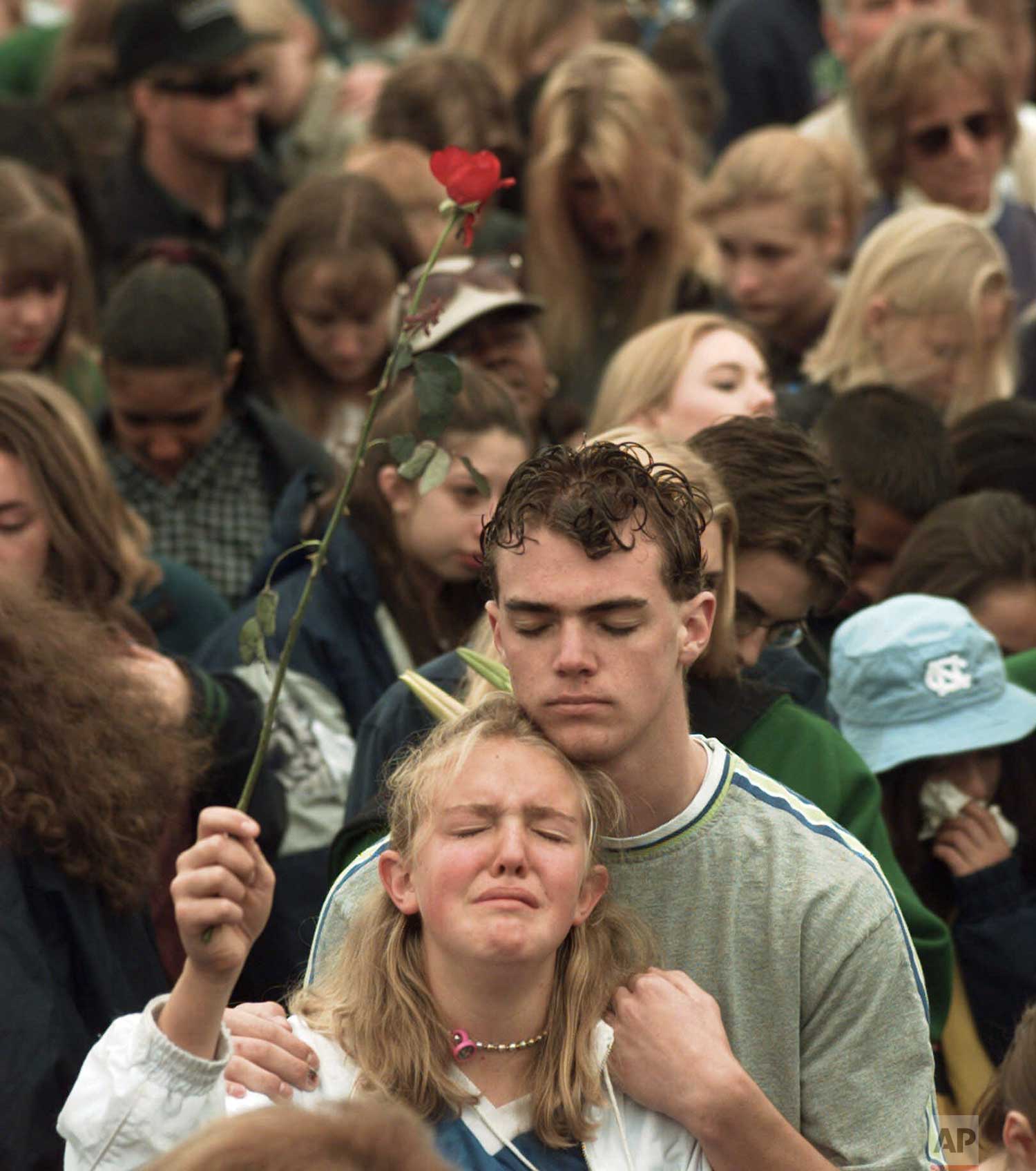  A young girl holds a rose  as she is held during prayer at a memorial service on Sunday, April 25, 1999, for the victims of the Columbine High School shooting rampage in Littleton, Colo. (AP Photo/Eric Gay) 