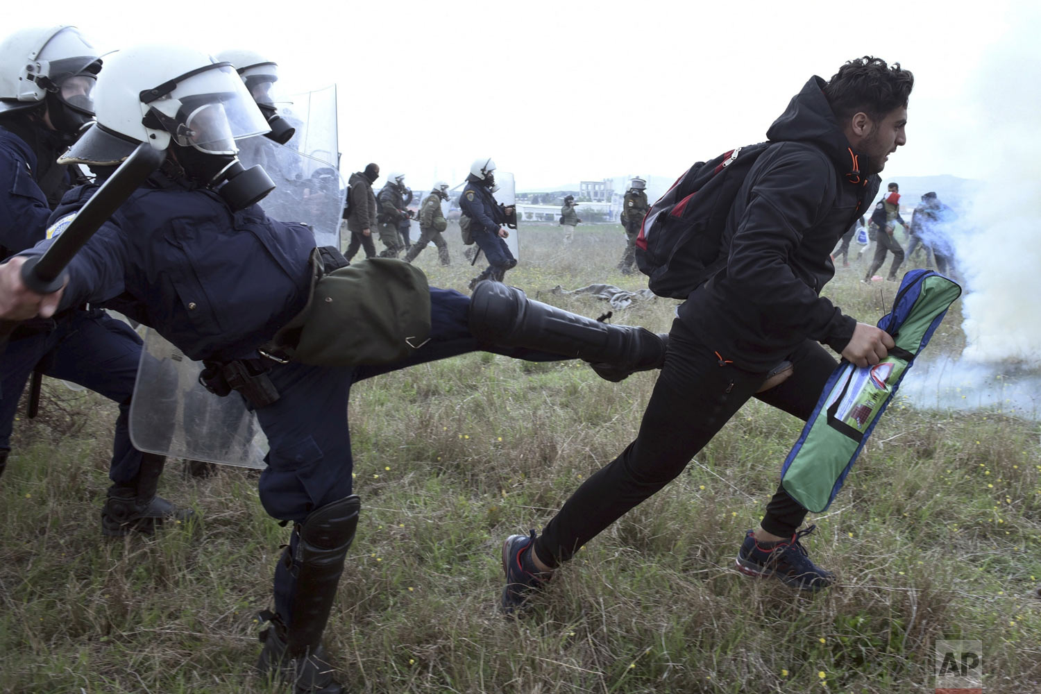 A police officer kicks a protesting migrant during clashes outside a refugee camp in the village of Diavata, west of Thessaloniki, northern Greece, Saturday, April 6, 2019. Clashes between hundreds of protesting migrants and police continued for a third day outside the overcrowded camp, with migrants throwing rocks at police and the police responding with tear gas and stun grenades. (AP Photo/Giannis Papanikos)