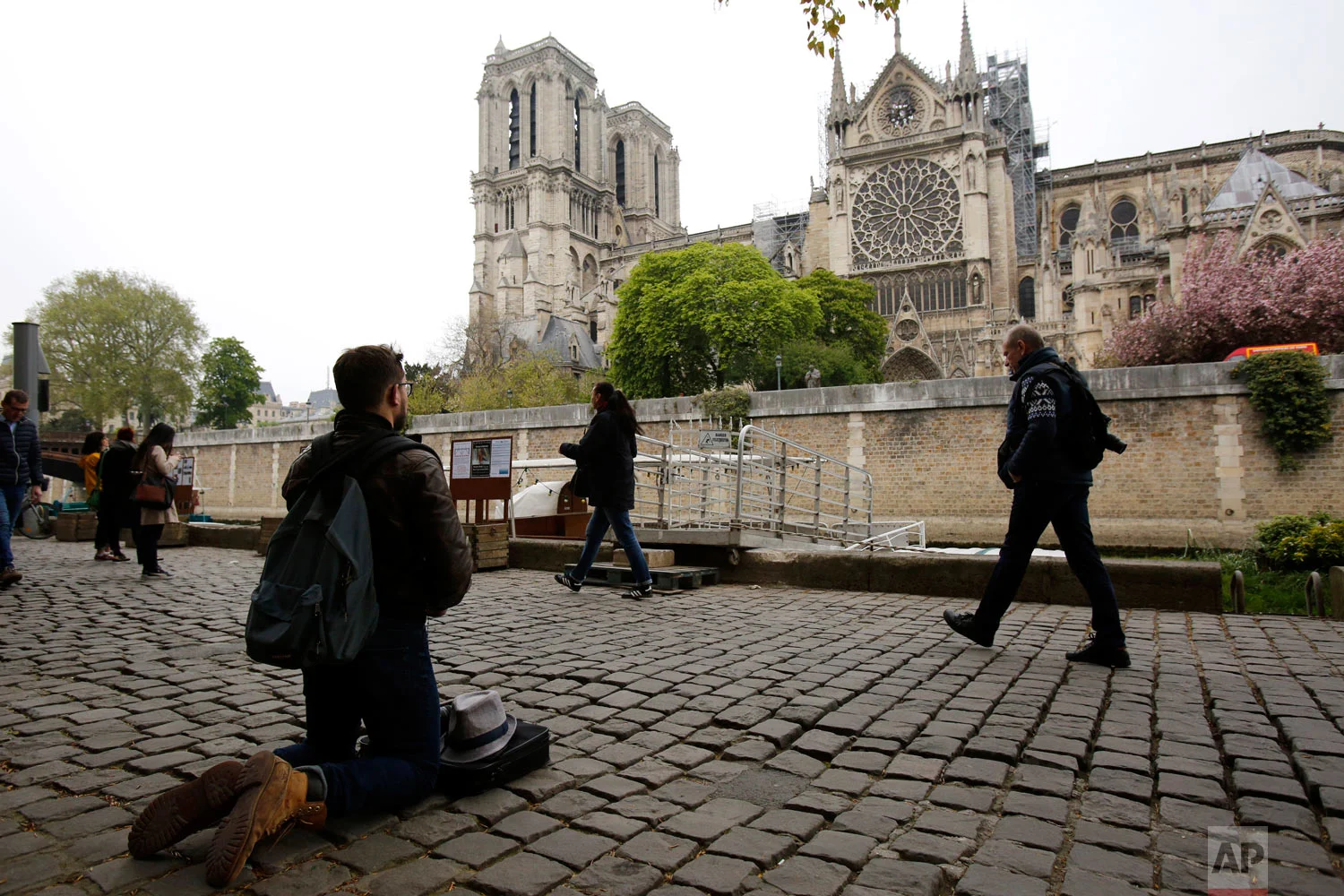 Man kneels as people came to watch and photograph the Notre Dame Cathedral after the fire in Paris, April 16, 2019. (AP Photo/Christophe Ena)