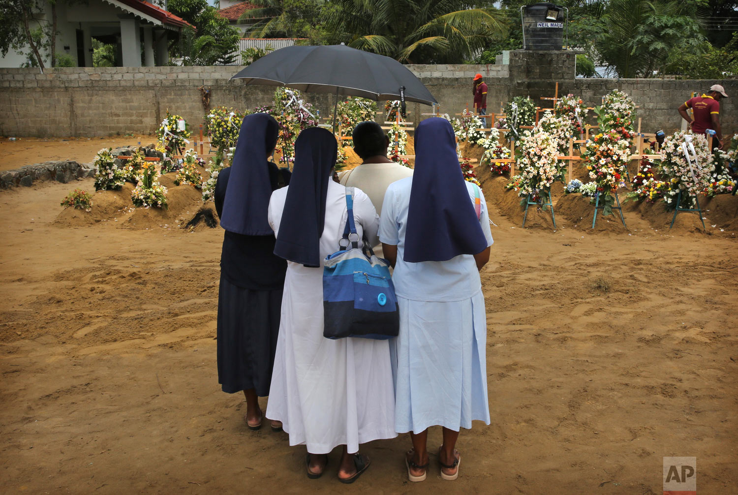 Catholic nuns stand with a relative of a victim of Easter Sunday's bomb blast at St. Sebastian Church at a mass burial site in Negombo, Sri Lanka, April 25, 2019. (AP Photo/Manish Swarup)