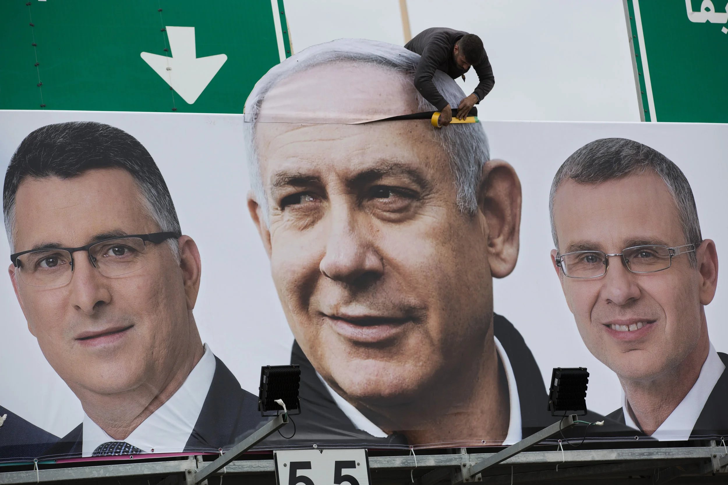 A man works on a Likud party election campaign billboard depicting Israeli Prime Minister Benjamin Netanyahu, center, and his party candidates, in Petah Tikva, Israel, Monday, April 1, 2019. (AP Photo/Oded Balilty)