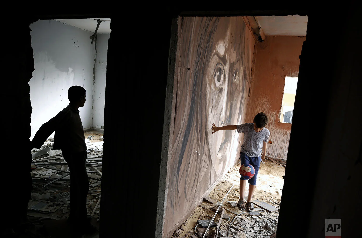 A boy plays football next to a mural painted by Palestinian artist Ali Al-Jabali in the remains of a building that was damaged during the 2014 war between Israel and Hamas, in Gaza City, Tuesday, April 30, 2019. (AP Photo/Hatem Moussa)
