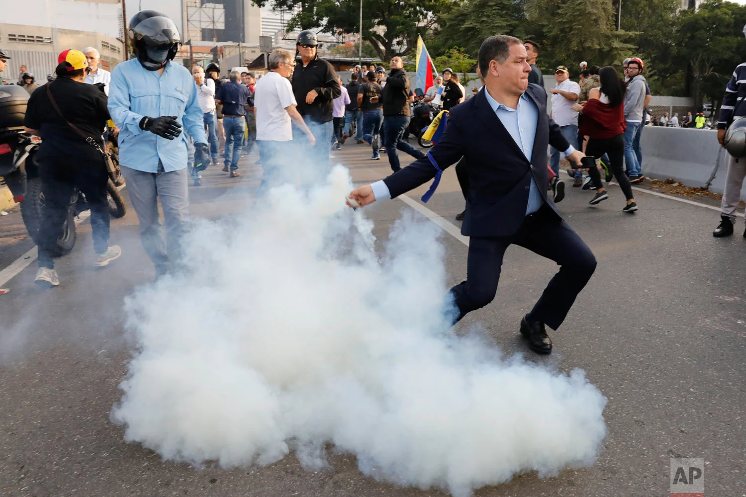 An opponent to Venezuela's President Nicolas Maduro returns a tear gas canister to soldiers who launched it at a small group of civilians and rebel troops gathered outside La Carlota air base in Caracas, Venezuela, April 30, 2019. (AP Photo/Ariana Cubillos)