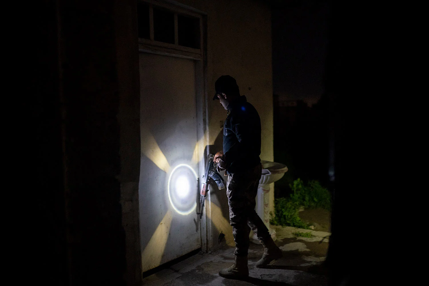 In this April 2, 2019 photo, an Iraqi army 20th division soldier uses his AK-47 riffle to knock on a door during a nighttime raid near Badoush, Iraq. (AP Photo/Felipe Dana)