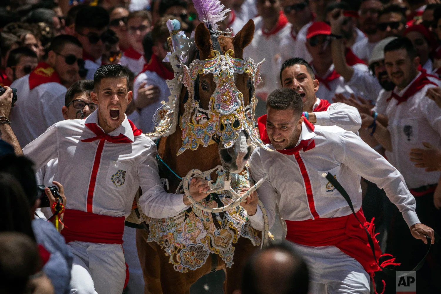 A troupe and their richly decorated horse make their way amid the crowd during the "Los Caballos del Vino," usually translated as the Running of the Wine Horses in Caravaca de la Cruz, southeast Spain, Thursday, May 2, 2019. (AP Photo/Bernat Armangue)