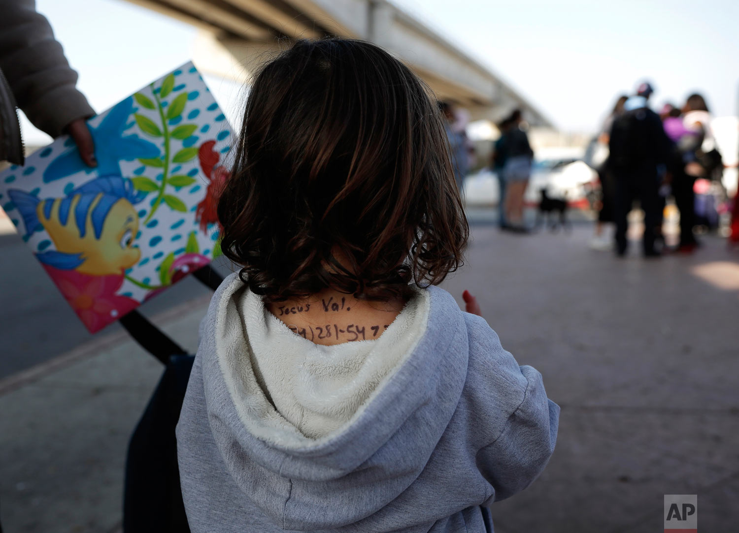 The back of a girl from the Mexican state of Michoacan displays a name and number, written in ink. She waits to apply for asylum in the United States with her mom and sister, in Tijuana, Mexico, April 25, 2019. Her mother said she wrote the information on her daughter because she feared losing track of the child if separated during the asylum application process. (AP Photo/Gregory Bull)