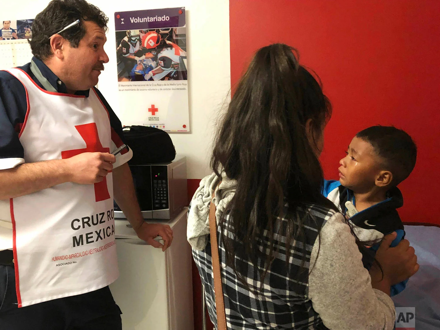Mexican Red Cross-Cruz Roja Mexicana technician Marco Antonio Mendoza, left, helps a mother and her 3-year-old son in Nogales, Mexico, April 15, 2019. (AP Photo/Patricio Espinoza)