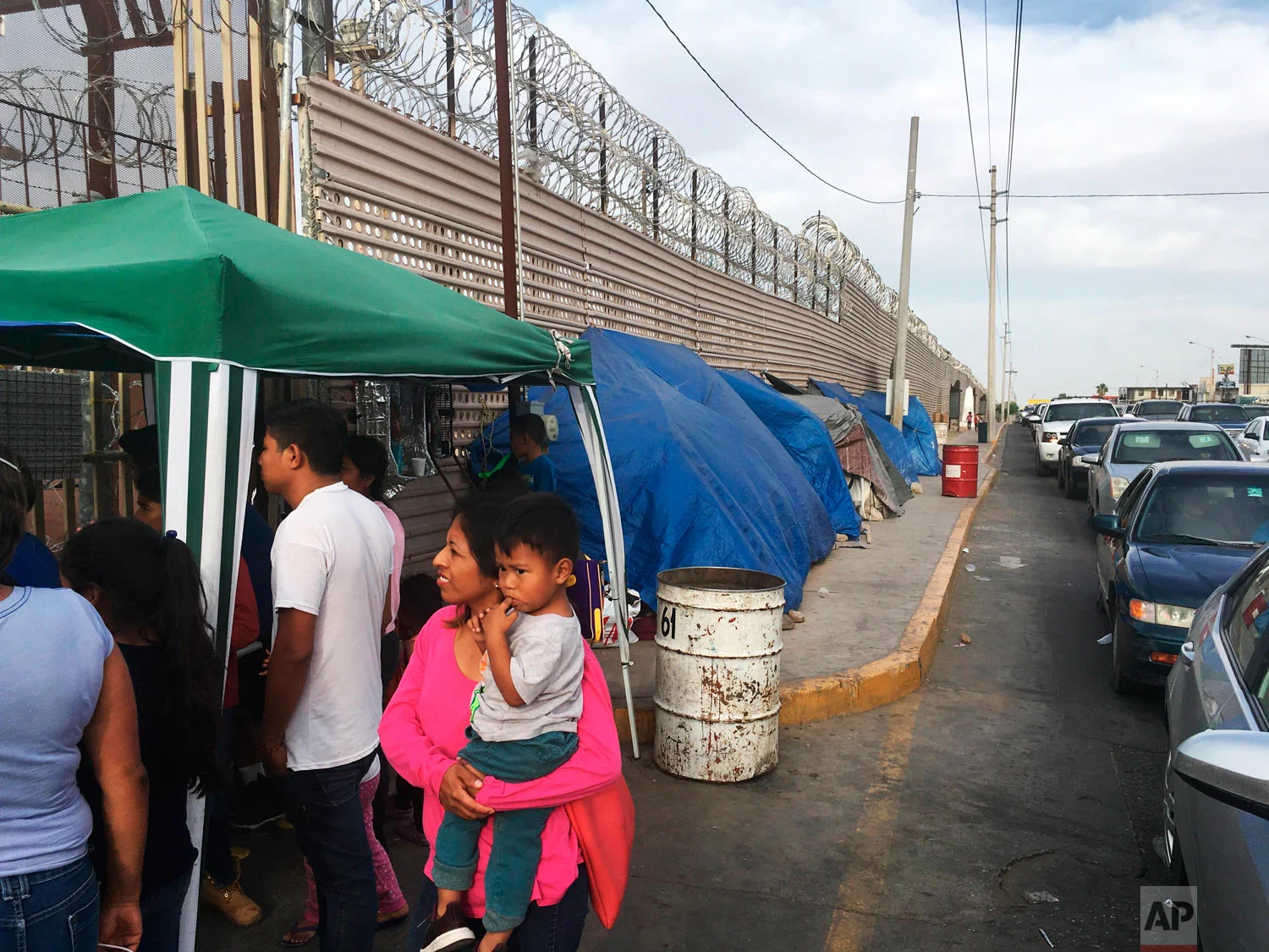 Migrants walk between tents, left, and cars waiting to cross the border in San Luis Rio Colorado, Mexico and Arizona, May 5, 2019. (AP Photo/Elliot Spagat)