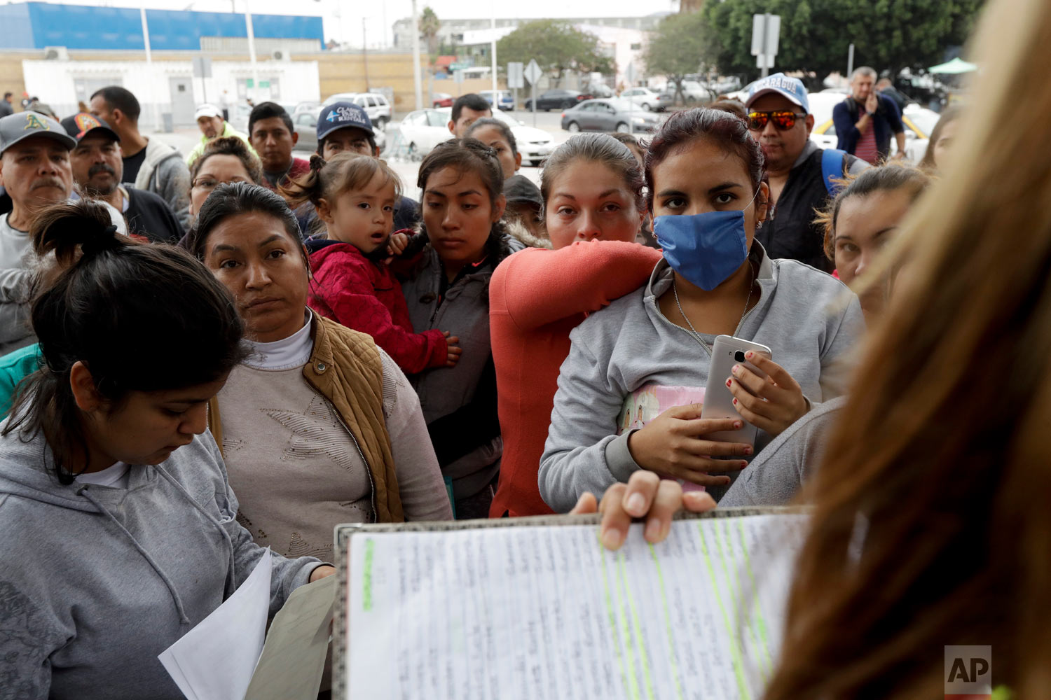 Women in Tijuana, Mexico, look on as numbers and names are called to from a list of asylum seekers. (AP Photo/Gregory Bull)