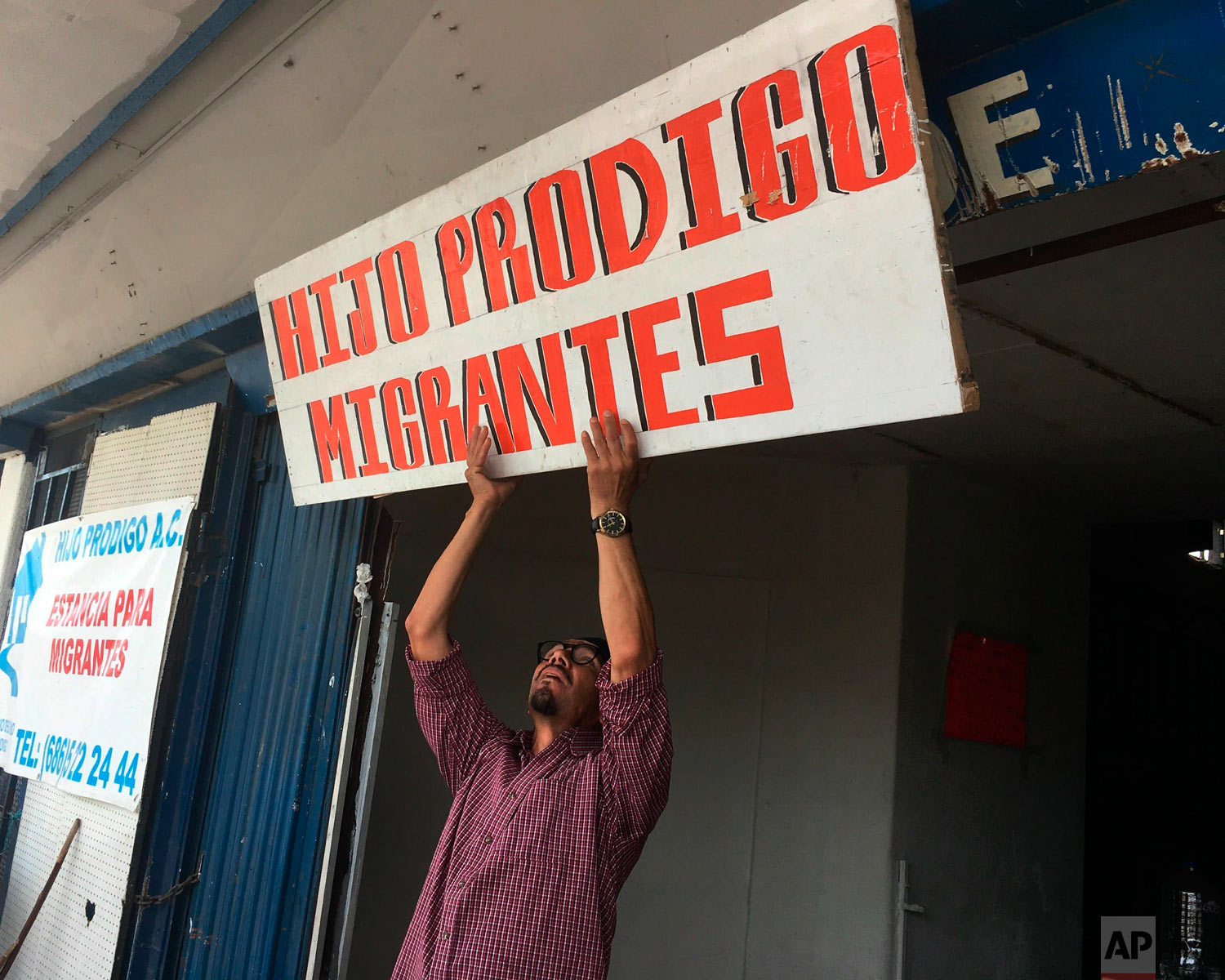 In this May 5, 2019, photo, Bernabe Rivera hoists a sign over a migrant shelter he manages in Mexicali, Mexico. (AP Photo/Elliot Spagat)